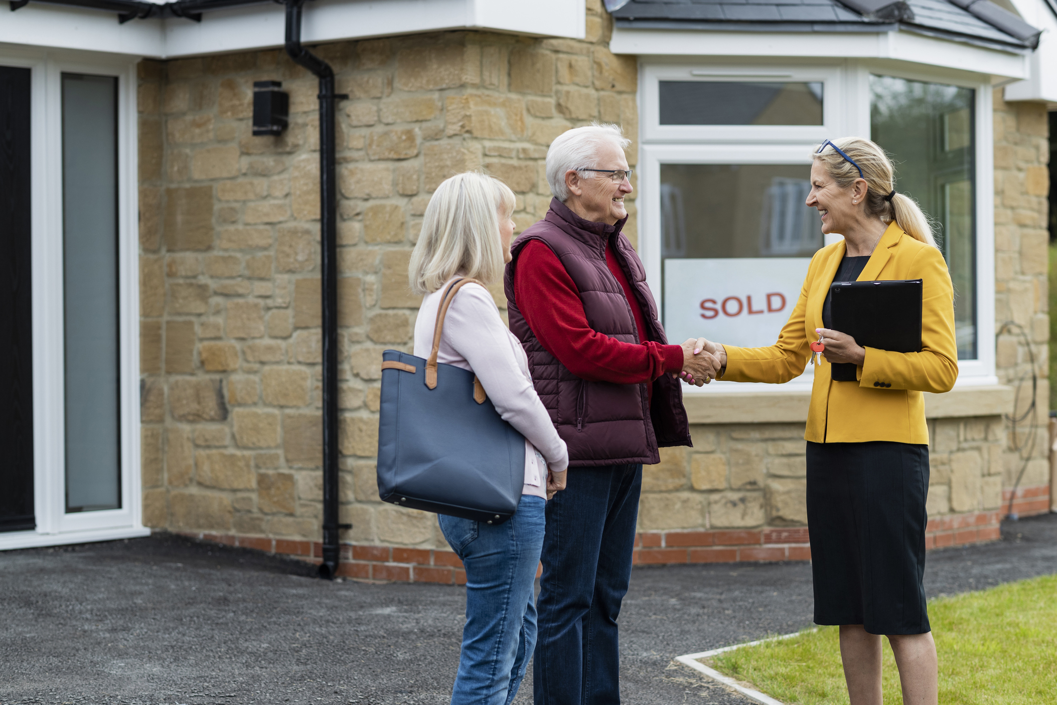older adult couple shaking hands with their realtor after selling their home.